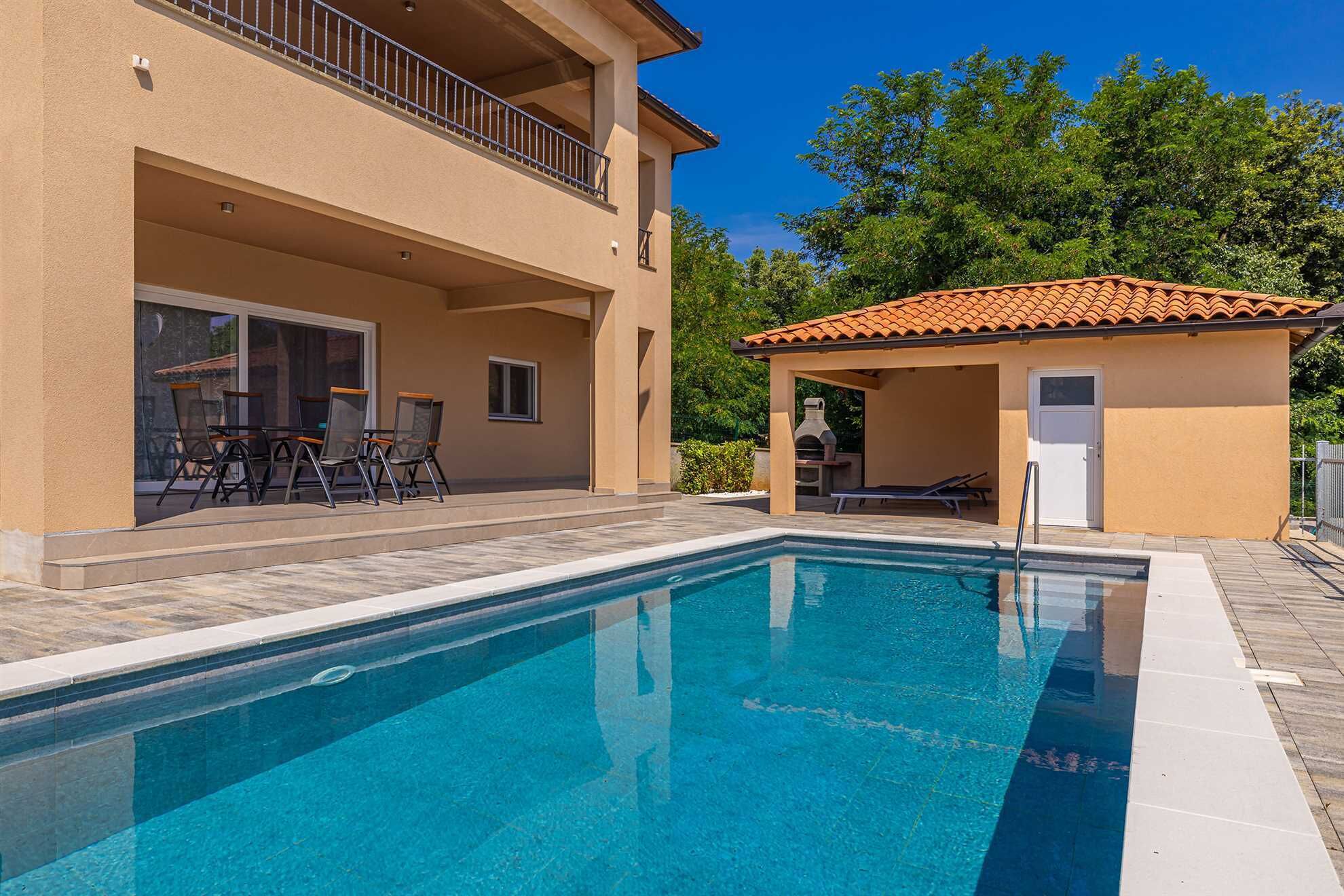 A swimming pool with a patio area, a covered barbecue area, and a two-story building with a balcony.