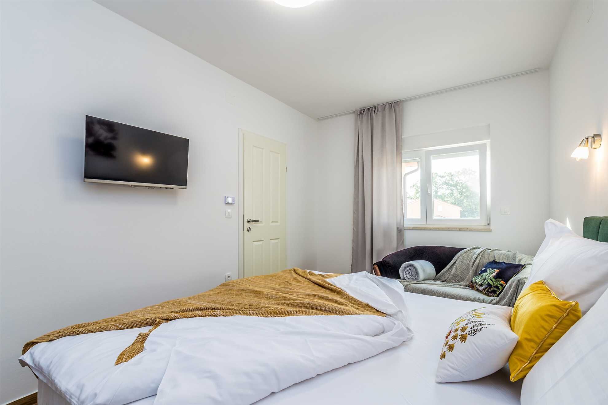 Un dormitorio con cama, televisor, ventana con cortinas y mesita de noche.