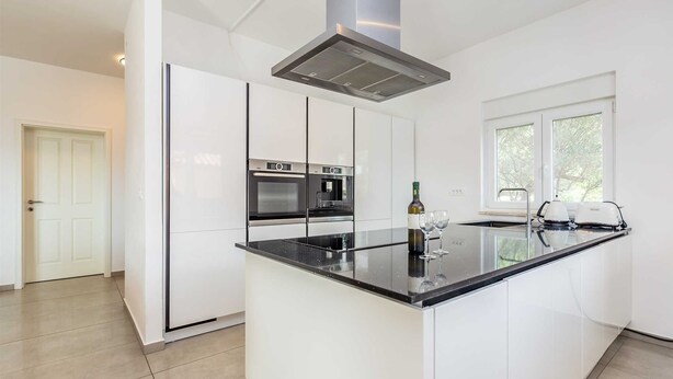 Una cocina moderna con armarios blancos, encimera negra, horno integrado y ventana que proporciona luz natural.