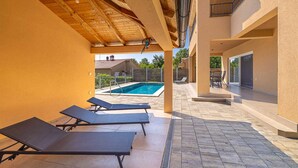 Un espacio exterior cubierto con piscina, sillones de descanso y una escalera que lleva a un nivel superior.