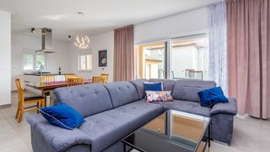 Una sala de estar moderna con un sofá seccional gris, una mesa de centro de vidrio y un comedor con sillas de madera y una mesa.