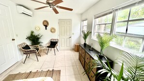 A room with a ceiling fan, a door, a window with a view, wicker chairs, a small table, and potted plants. - CAICOSVERDE Amazing Garden 2 Bedrooms Suite with Living Room and Kitchenette. (Providenciales)