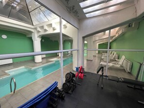 An indoor swimming pool with a gym area, green walls, and a large window.