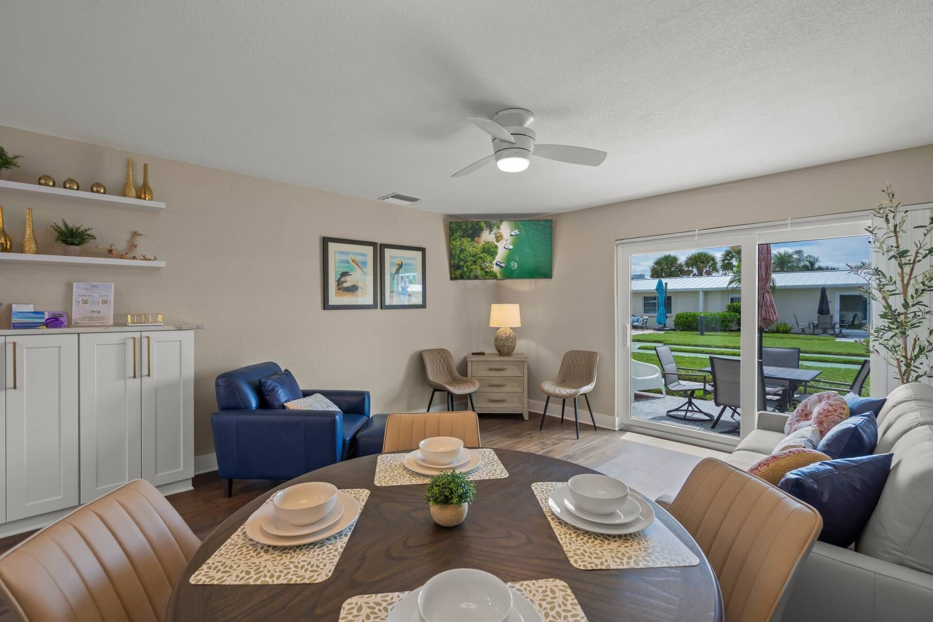 A dining area with a table set for four, a ceiling fan, and a view of the outdoors.