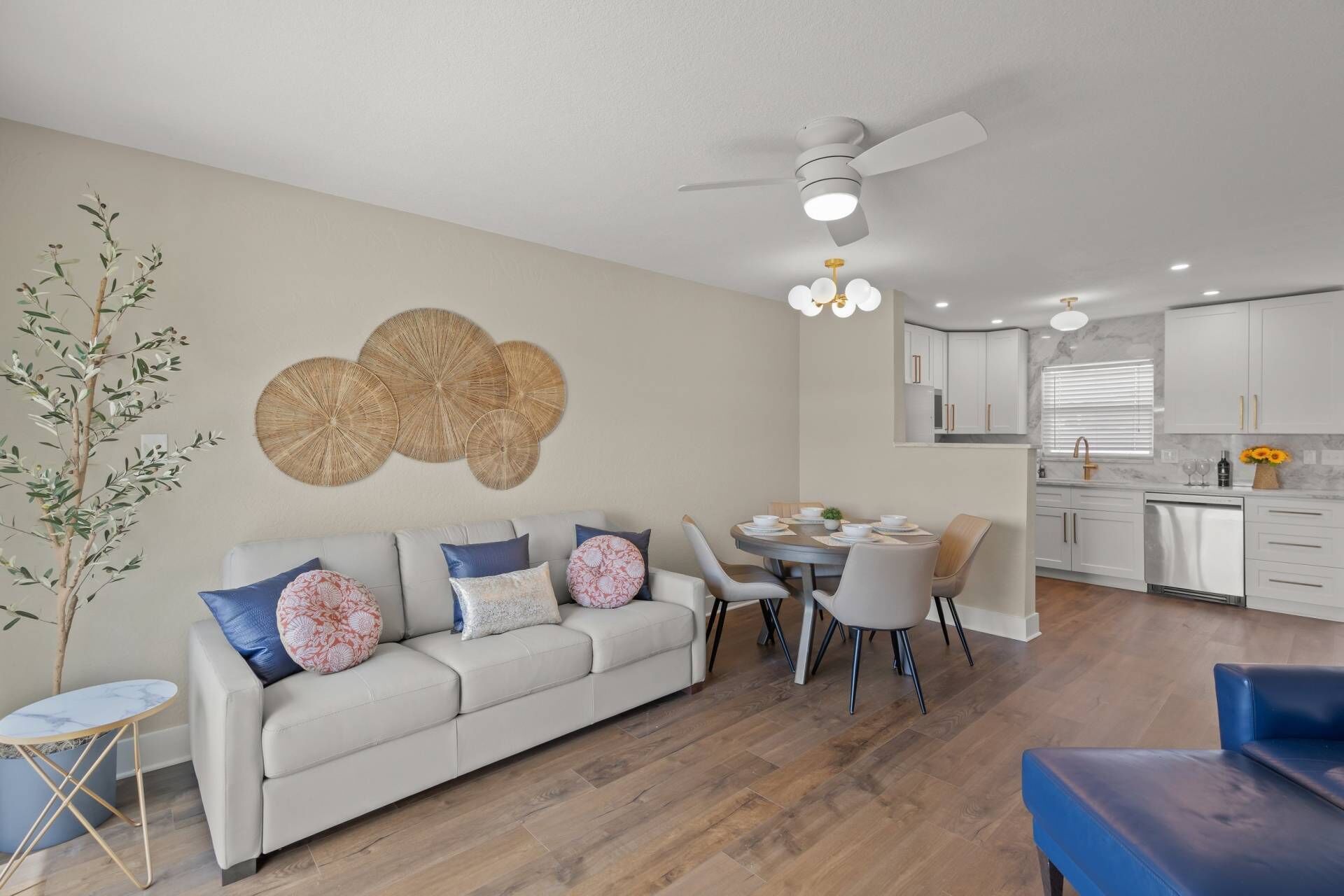 Una sala de estar moderna con sofá, mesa de comedor y sillas. Cuenta con una zona de cocina con gabinetes y un lavamanos.