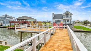 A waterfront property with a wooden deck, a pool, and a large house with a balcony. - Waterfront Canal Home with Pool & Fishing Access (Galveston)