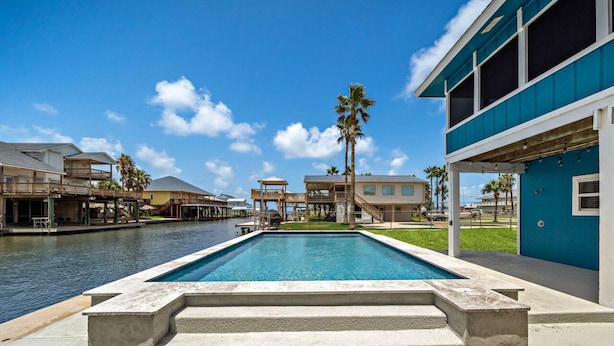 A swimming pool with a view of a canal and buildings in the background. - Waterfront Canal Home with Pool & Fishing Access (Galveston)