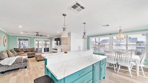 A spacious living area with a kitchen island, a dining table with chairs, and a seating area with a sofa and chairs. - Waterfront Canal Home with Pool & Fishing Access (Galveston)