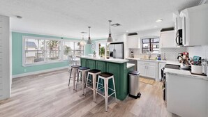 A modern kitchen with a central island, bar stools, and a view of the outdoors. - Waterfront Canal Home with Pool & Fishing Access (Galveston)