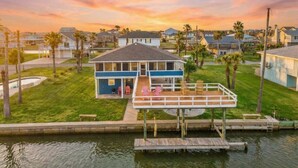 A waterfront house with a dock, a covered deck, and a grassy yard. - Waterfront Canal Home with Pool & Fishing Access (Galveston)