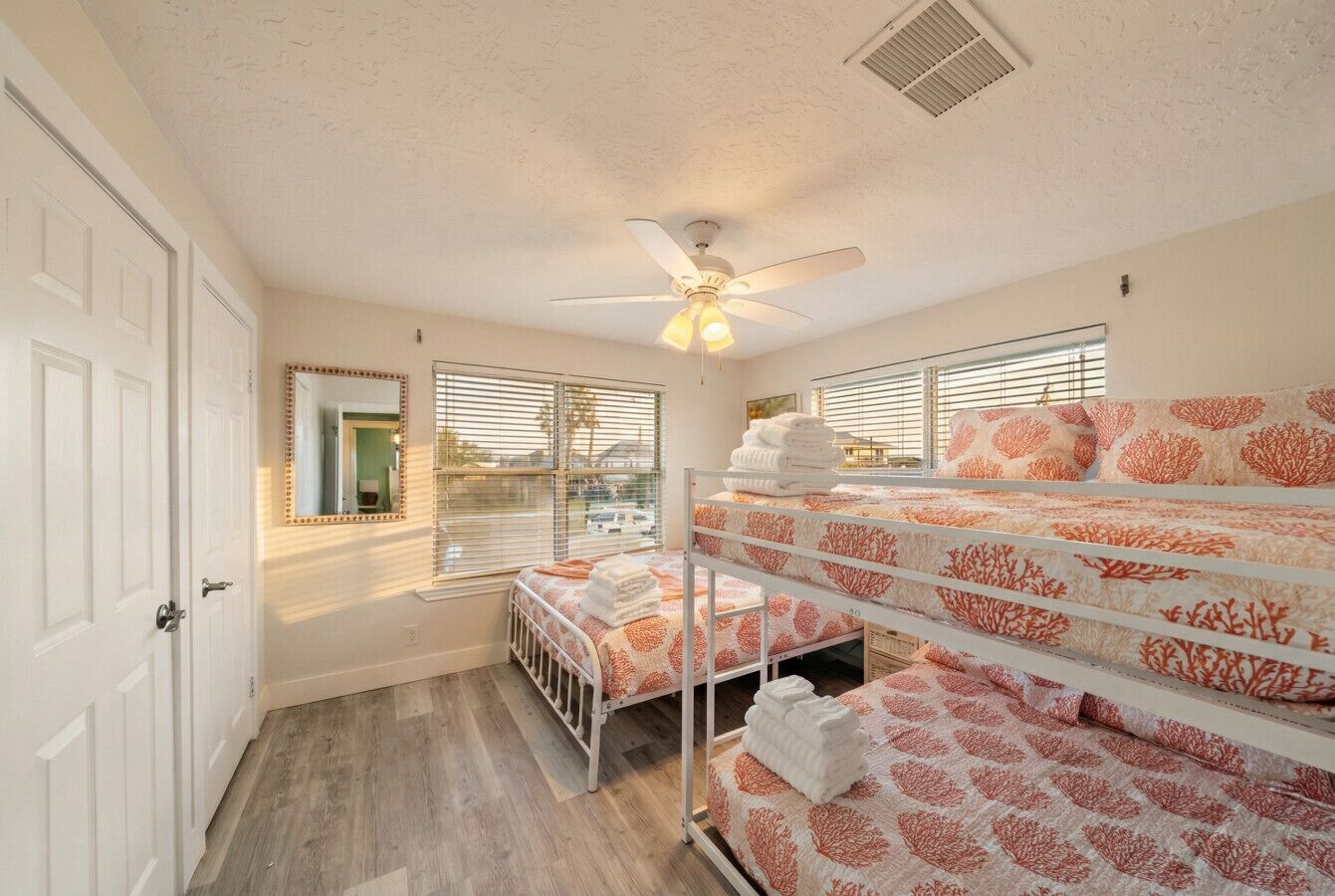 Une chambre avec des lits superposés, un ventilateur de plafond et une vue sur l’extérieur par les fenêtres.