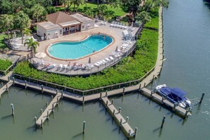 Luftaufnahme eines Resorts mit einem zentralen Schwimmbad, umgeben von Liegestühlen und einem Steg mit einem Boot.