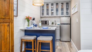 Una cocina compacta con una isla central, dos taburetes de bar, una lámpara colgante y un refrigerador.