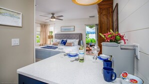 Habitación de hotel con cama, zona de comedor con mesa y sillas, cocina equipada con refrigerador y vistas al exterior.