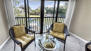 A balcony with wicker chairs, a glass table, and a view of a water body and greenery. - White Sands & Ocean Waves Bld 5 2nd fl (Siesta Key)