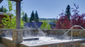 A stone hot tub with a metal ladder, surrounded by stone walls, set against a backdrop of trees and a building. - Stunning Winter Park Condo Near Slopes! (Winter Park)