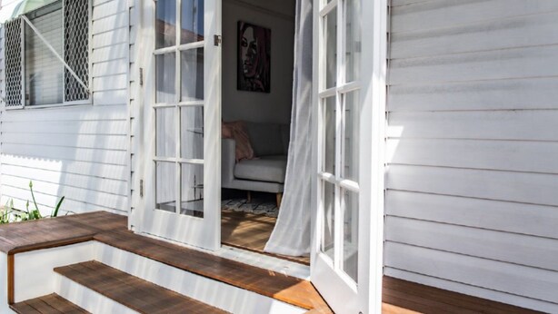 A white wooden house with a front door open, revealing a grey sofa inside.