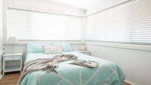 A bedroom with a bed, a nightstand, a lamp, and a window with blinds.