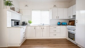 A modern kitchen with white cabinets, a microwave, a coffee maker, a sink, and a stove.