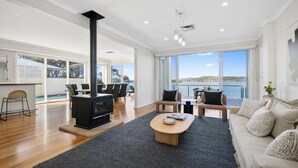 A modern living room with a black wood-burning stove, a sofa set, a coffee table, and a view of the sea through large windows. - Stay 3 nights, pay 2 this Winter* (POINT CLARE)
