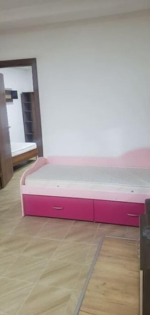 A bedroom with a pink bed, a wooden floor, and a white wall.