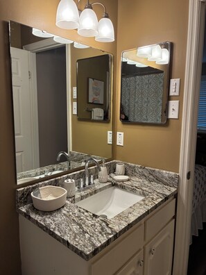 Une salle de bain avec un lavabo en marbre, deux miroirs, un porte-serviettes et un luminaire placé au-dessus des miroirs.