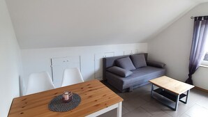 A modern living space with a dining table, white chairs, a grey sofa, and a small side table.