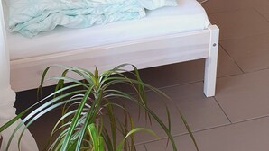 A neatly made bed with a geometric patterned pillow, a small potted plant on a bedside table, and a similar plant on a side table.