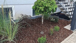 A building with a paved entrance area, a small garden with mulch and plants, and a staircase with metal railings.