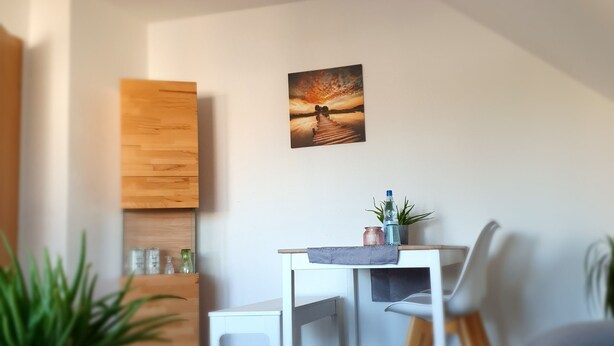 A modern living room with a dining area, featuring a wooden cabinet, a painting, and a potted plant.