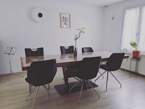 Ein Konferenzraum mit einem Holztisch, schwarzen Stühlen, einem Blumentopf, einem gerahmten Bild und einem Notenständer.