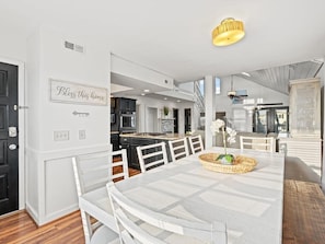 A modern kitchen with white cabinetry, a dining area with a white table and chairs, and a staircase leading to an upper level.