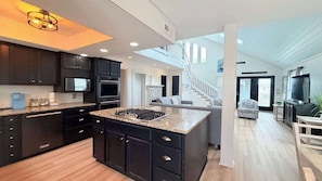 A modern kitchen with dark cabinetry, a granite island, and a built-in stove.