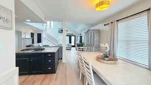 Een moderne keuken met een centraal eiland, een zithoek met tafel en stoelen, en een groot raam met zonwering.