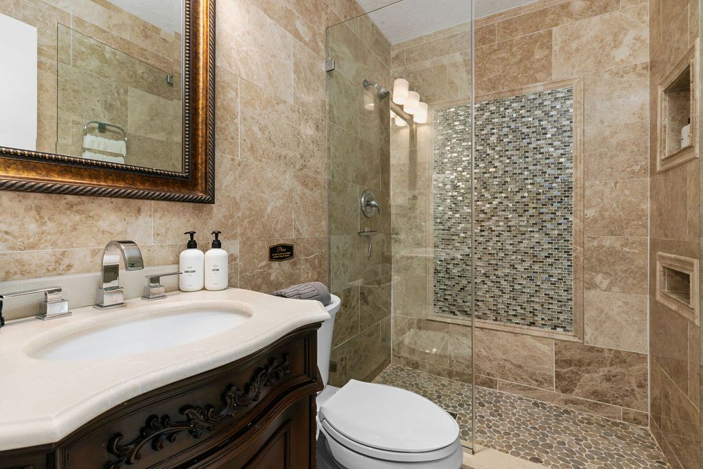 Un bagno con lavabo in marmo, box doccia in vetro e parete doccia rivestita in mosaico.