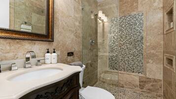 Un bagno con lavabo in marmo, box doccia in vetro e parete doccia rivestita in mosaico.