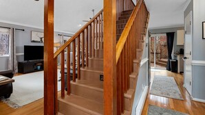 A wooden staircase leading to a second floor, a flat-screen TV, and a dining area with a table and chairs.