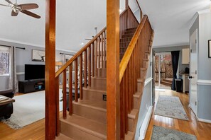 Una escalera de madera que conduce a un segundo piso, un televisor de pantalla plana y un comedor con mesa y sillas.