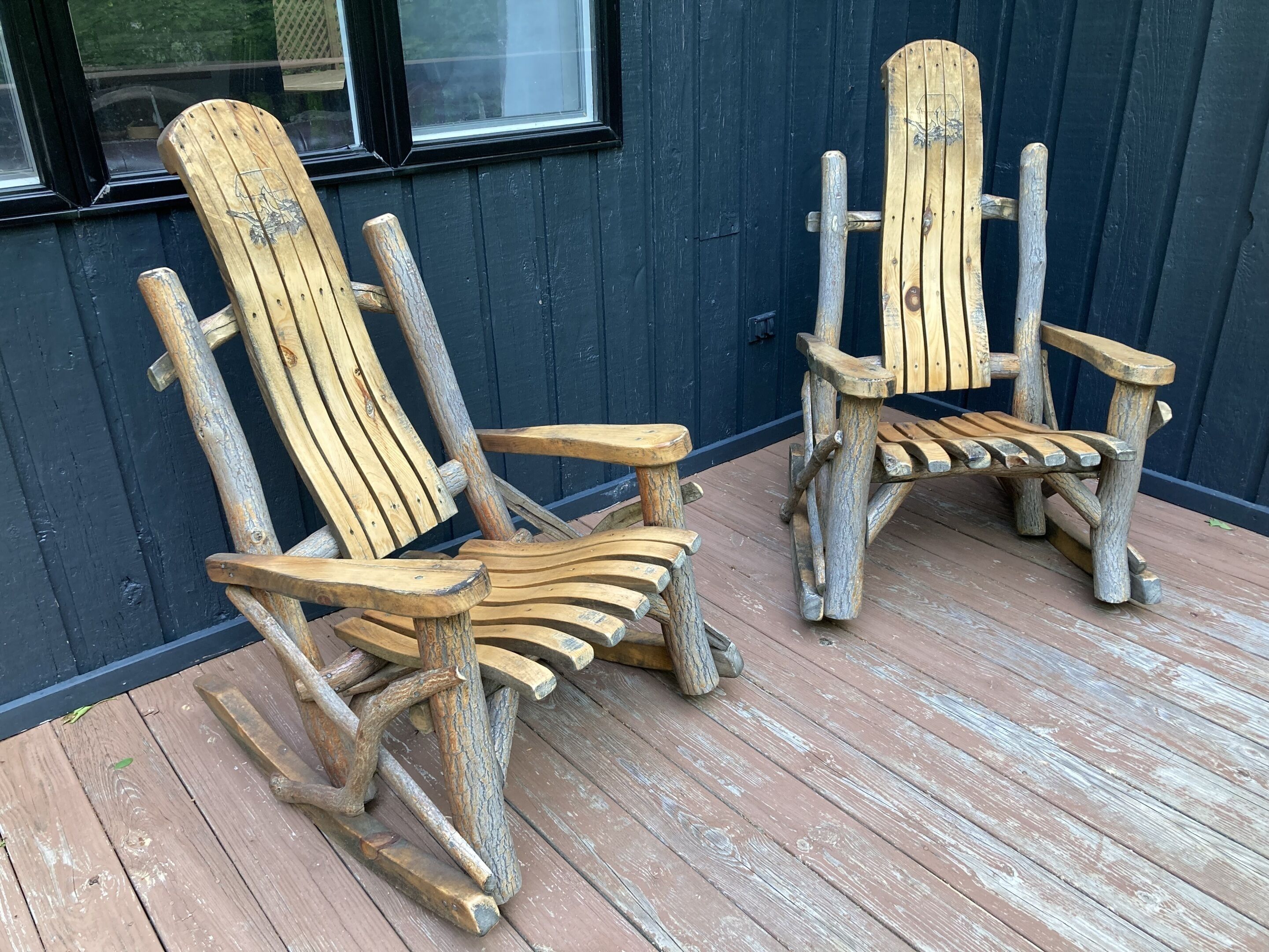 Two rustic Adirondack chairs made of wood, placed on a wooden deck.