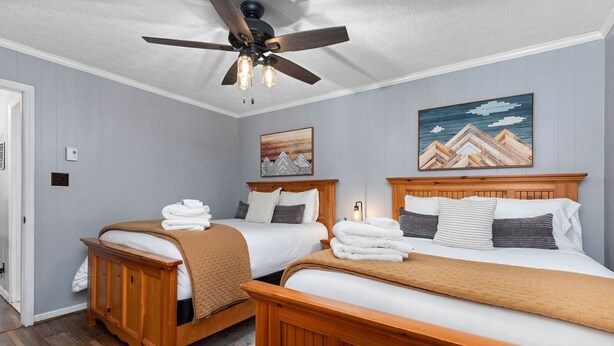 Quarto de hotel com duas camas de madeira, um ventilador de teto e obras de arte nas paredes.