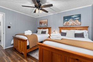 Una camera d'albergo con due letti in legno, una ventola a soffitto e opere d'arte alle pareti.