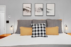 Ein ordentlich eingerichtetes Schlafzimmer mit einem Bett, drei gerahmten Bildern an der Wand und zwei Nachttischlampen.