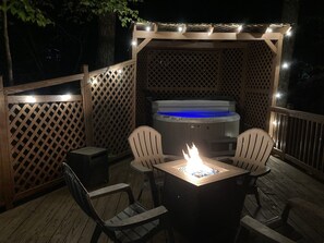Eine Terrasse im Freien mit Whirlpool, Feuerstelle und zwei Stühlen.