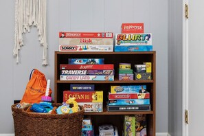 Ein Bücherregal mit verschiedenen Gesellschaftsspielen, ein Korbwäscher mit Spielzeug und ein Wandbehang aus Makramee.