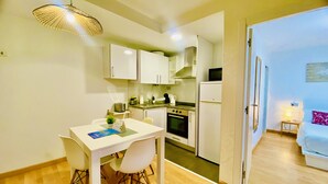A compact kitchen with white cabinets, a dining table with chairs, a microwave, a kettle, and a refrigerator. - San Francisco Home II by Gloove (Alicante / Alacant)