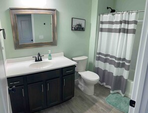 A bathroom with a white sink, dark cabinets, a toilet, and a shower curtain with black stripes. - 100 Acre Relaxing Retreat Near ARK- The Woodlands (Williamstown)