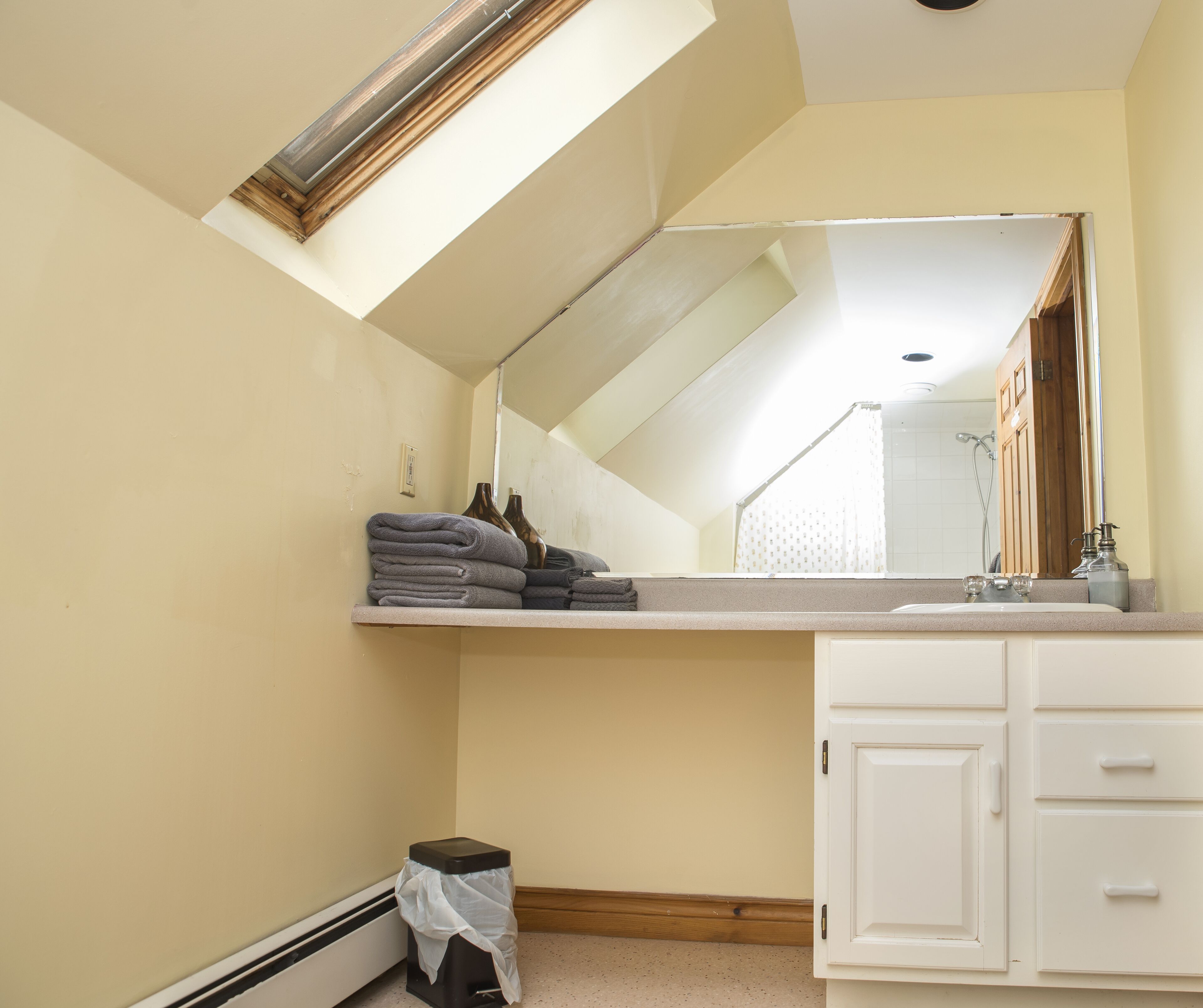 A bathroom with a skylight, a large mirror, a sink, and a cabinet.