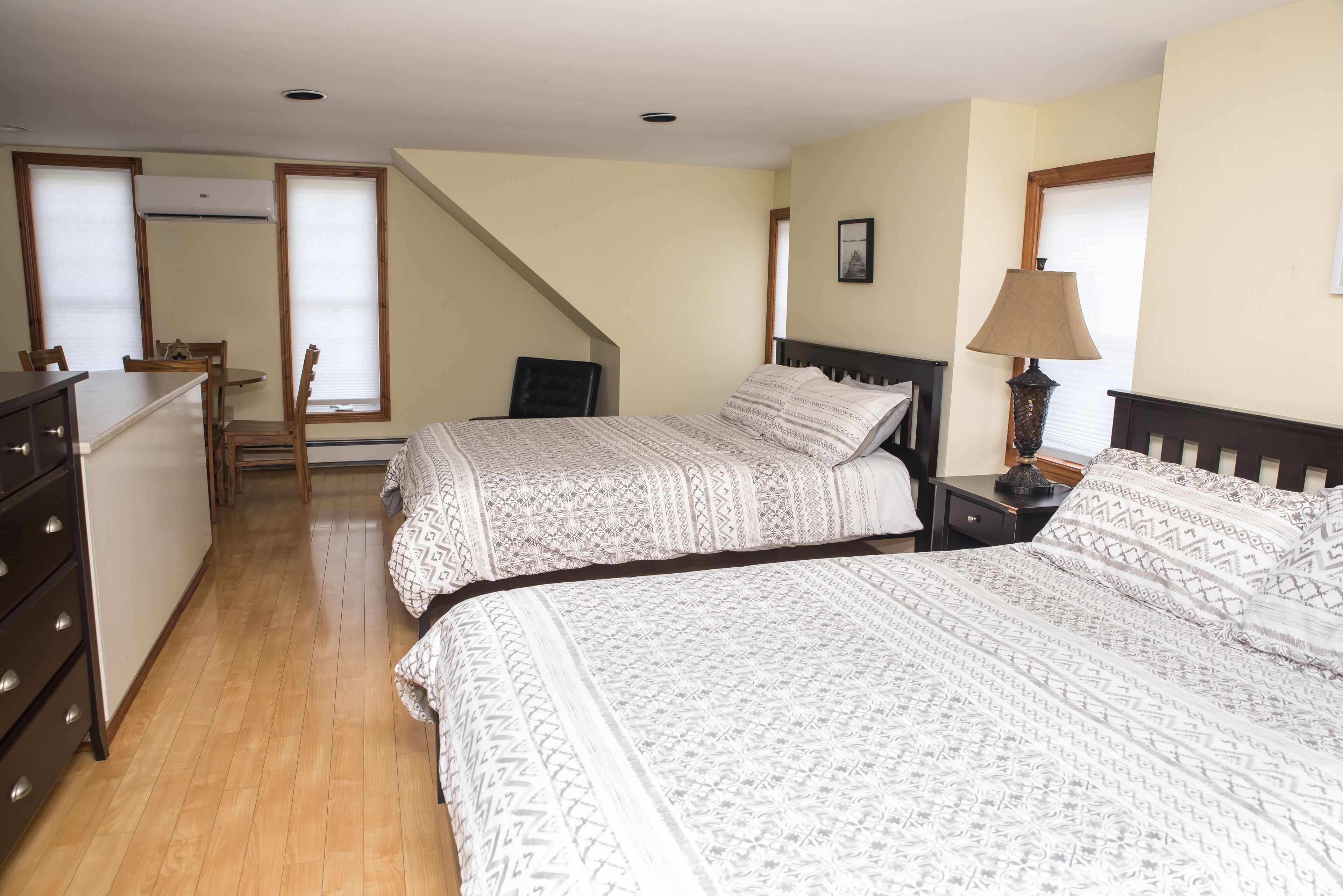 A bedroom with two beds, a desk, and a chair. There is a staircase leading to another room.