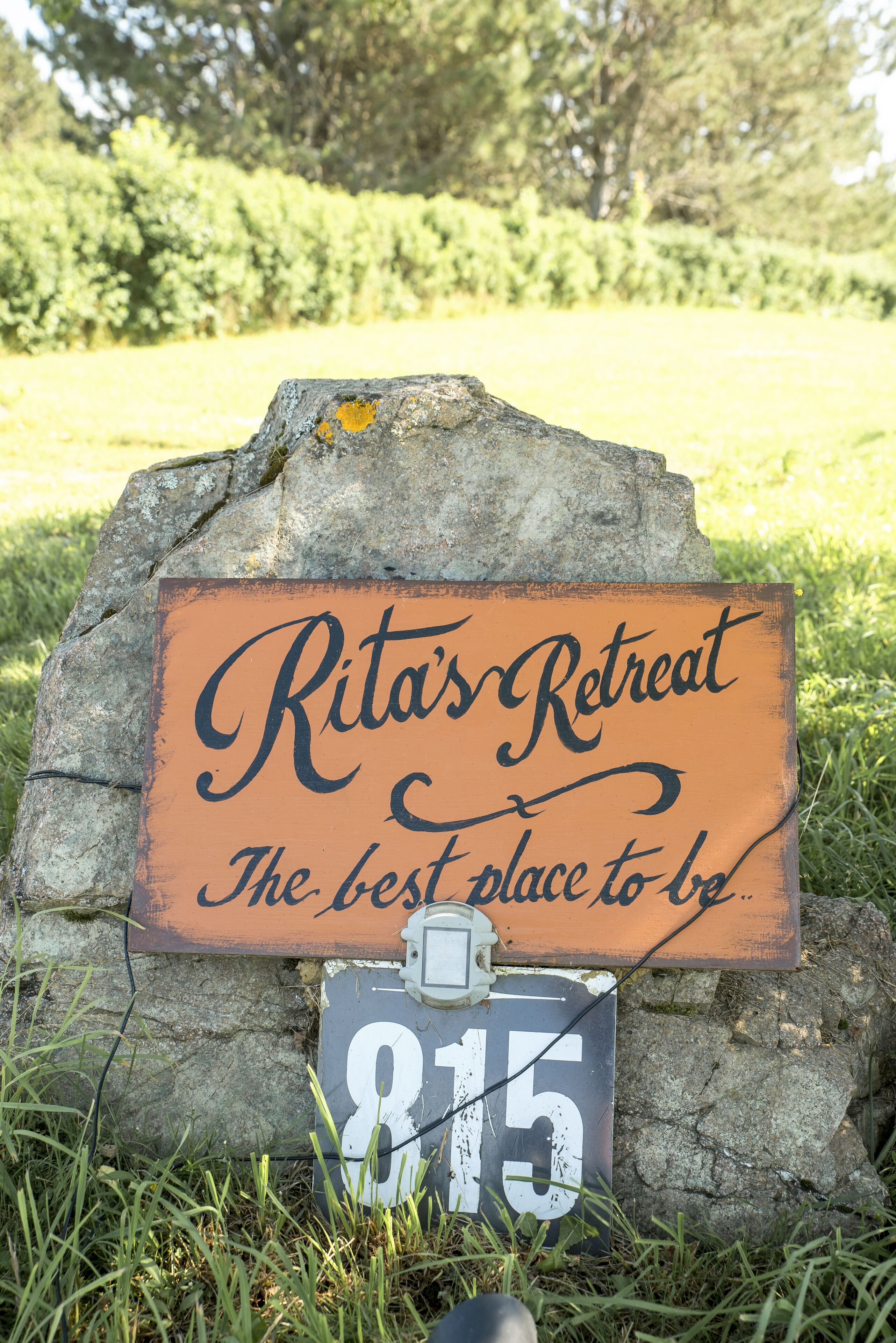 A rustic wooden sign with the text 'Rita's Retreat' and 'The best place to be' on a stone backdrop.