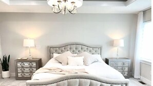 Ein Schlafzimmer mit einem mit Wirbeln versehenen Kopfteil, zwei Nachttischen mit Lampen, einer Topfpflanze und einer Kronleuchter.